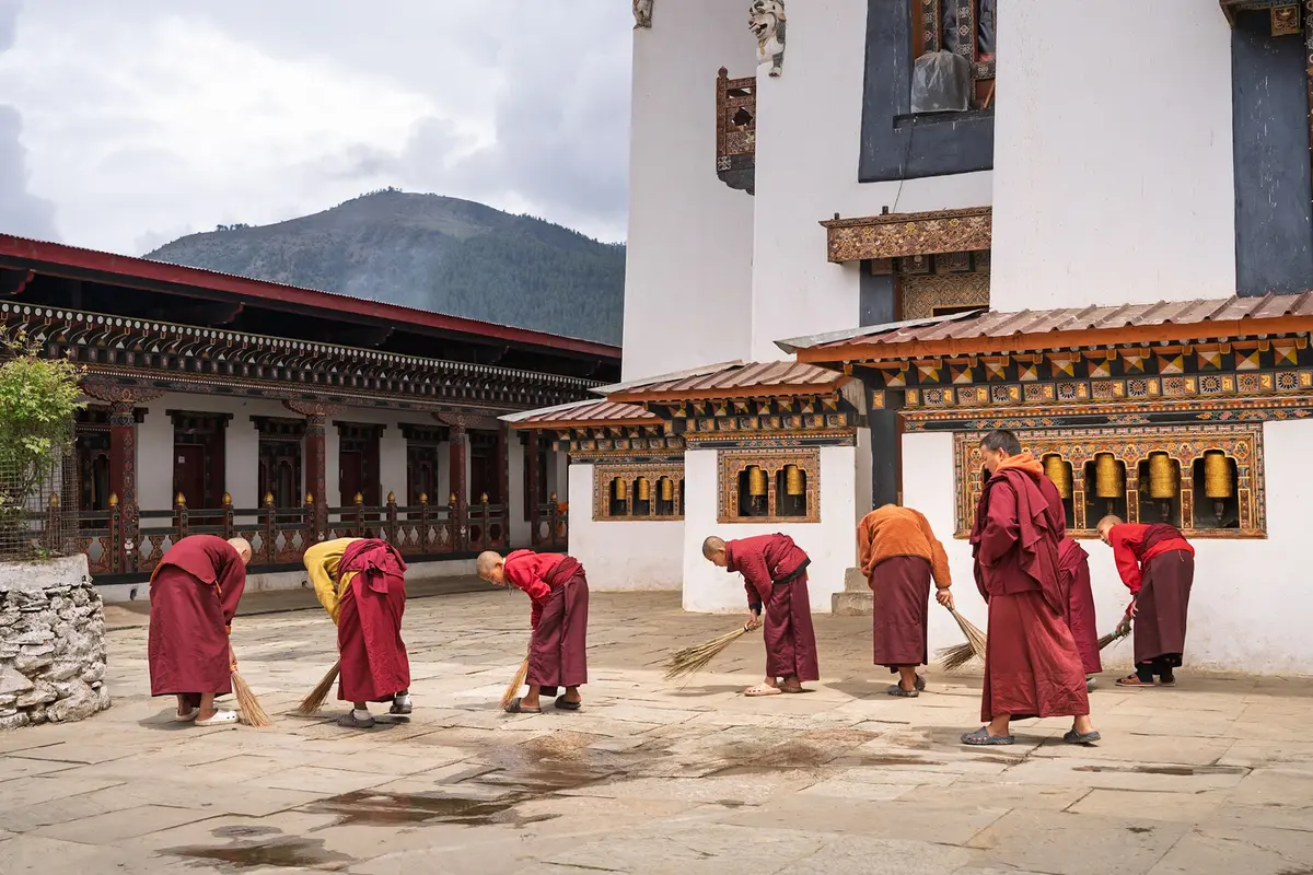Monks sweeping the courtyard of a Bhutanese monastery — the daily community practice that embodies the GNH principle of time balance and spiritual wellbeing