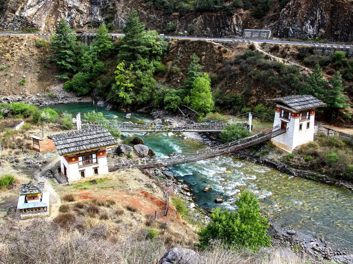 Traditional Bhutanese cantilever bridge spanning a river gorge — the Trans Bhutan Trail crosses dozens of these historic bridges connecting villages